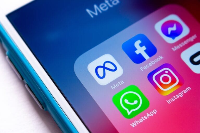 Ekran smartfona z ikonami aplikacji Meta, Facebook, Messenger, WhatsApp i Instagram na niebieskim i różowym tle.