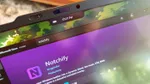 Close-up of a laptop screen showing a black notch overlay with a battery icon and time display above the Microsoft Store page for the Notchify app.